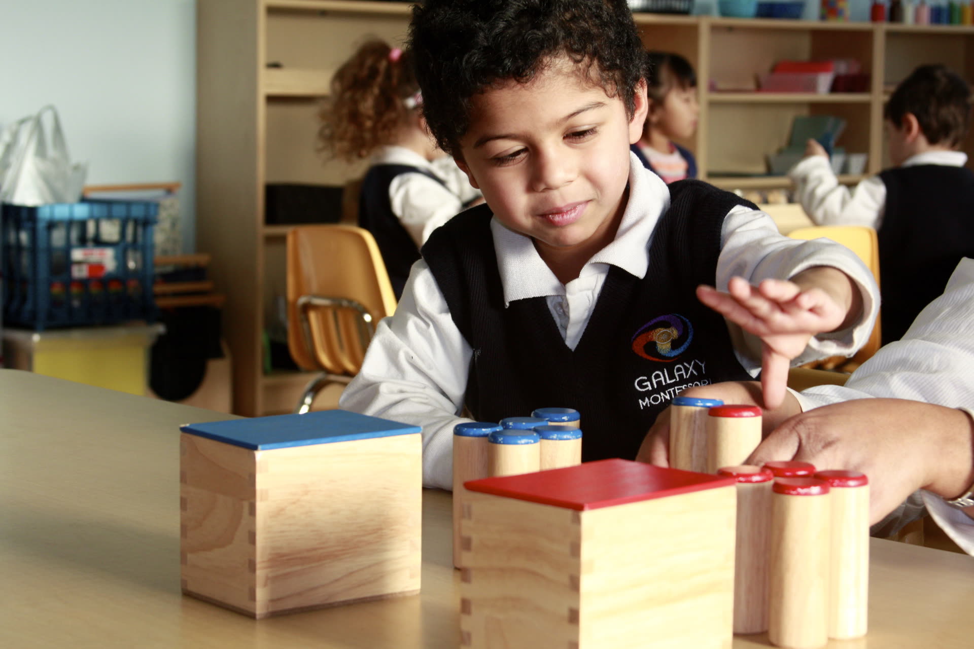 A Galaxy Montessori student working with wooden sensorial materials beside a teacher